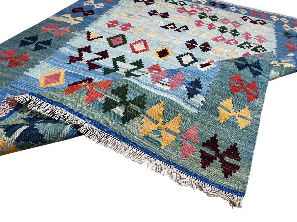Kelim-Teppich in Blau mit buntem Muster und Fransen, diagonale Ansicht über die Kante