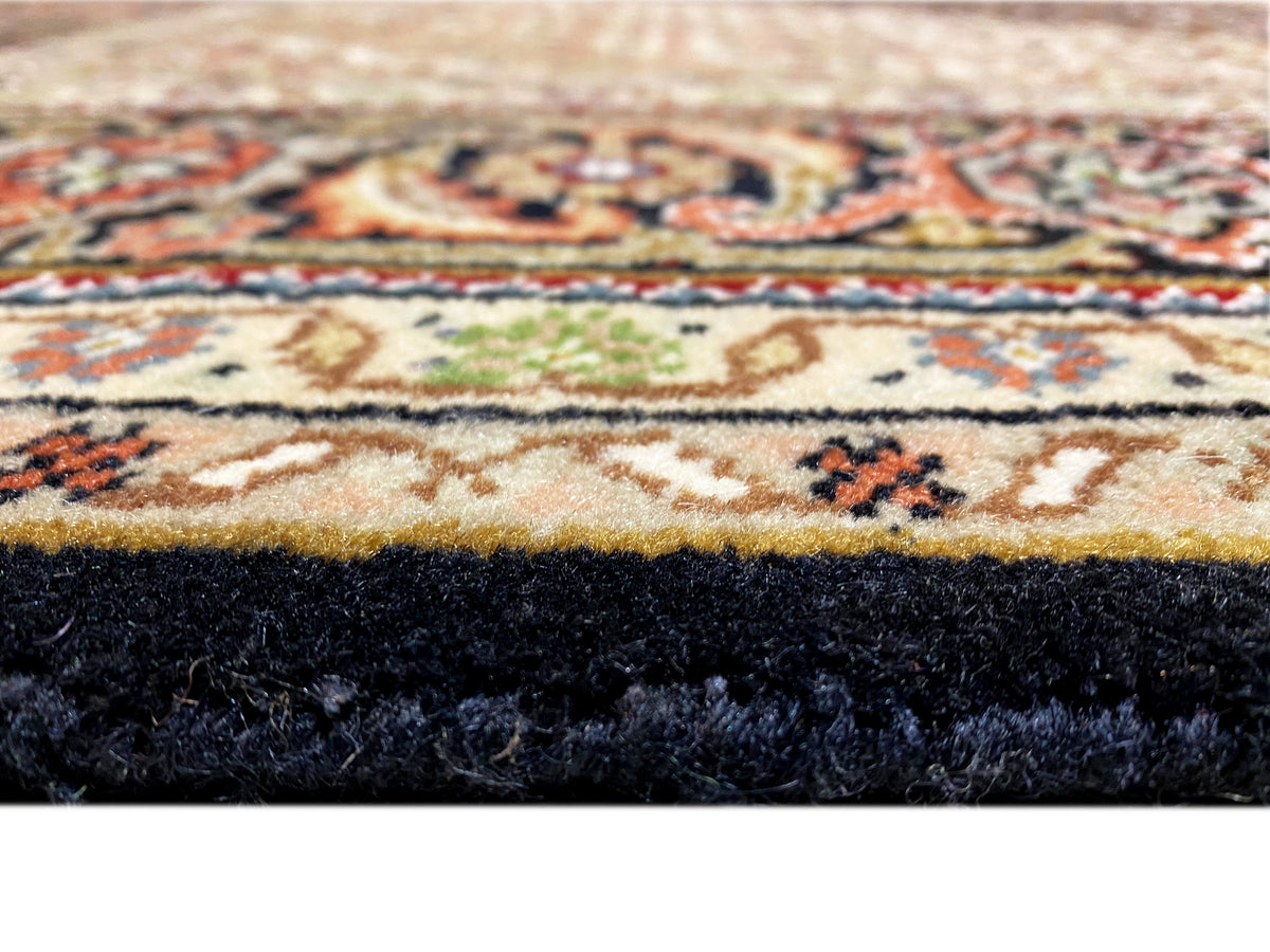 Teppichsaum im Detail mit dunklem Flor und mehrfarbiger Ornamentbordüre, Fransenbereich.