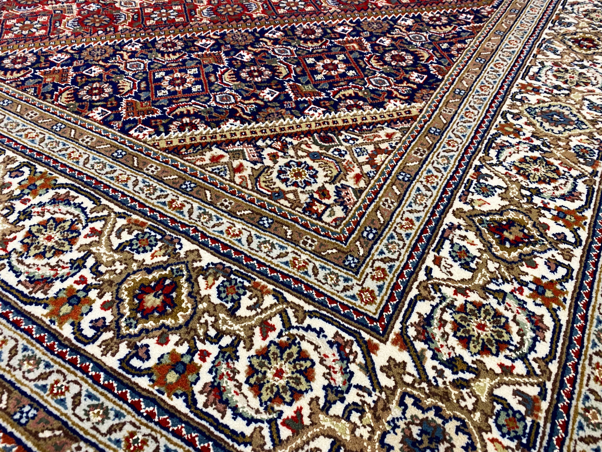 Nahansicht: Teppich mit blau-weißem Rahmen, roten Feldern und detailreichen Ornamenten