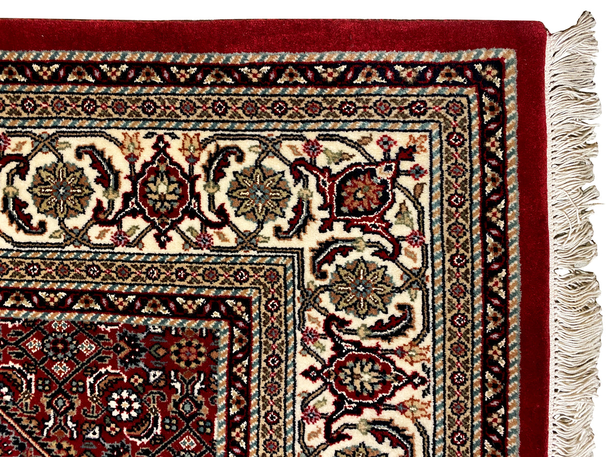 Teppichdetail mit rotem Grund, mehrfarbiger Bordüre und gewebtem Rand