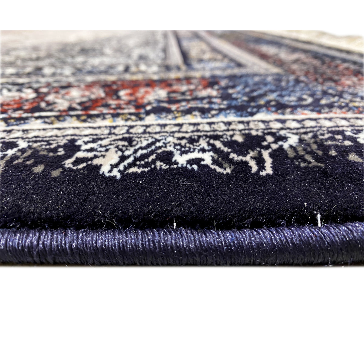 Teppich-Detail am Rand: Fransen und dunkler Flor, darüber Ornamentstreifen in Grau und Blau