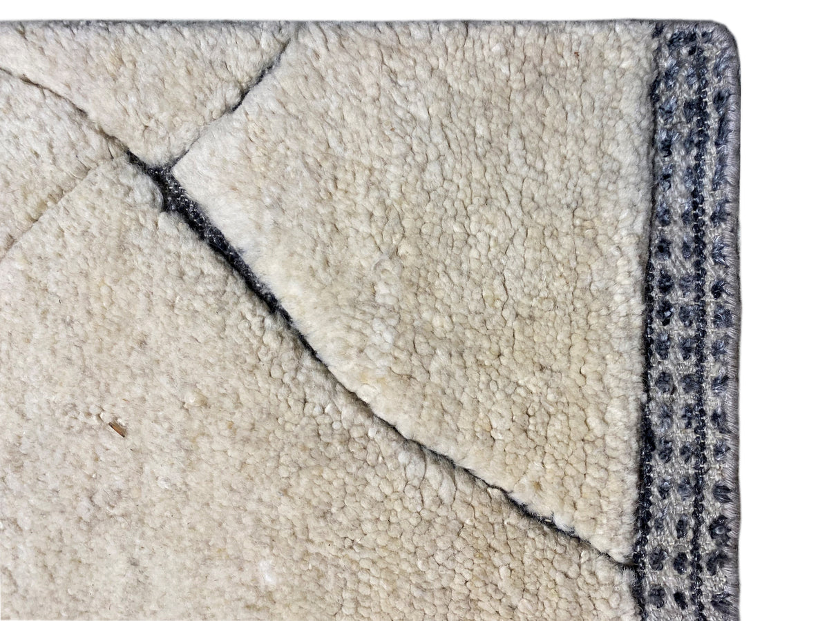 Detailaufnahme der Teppichkante: cremefarbener Flor mit blauer Zierborte