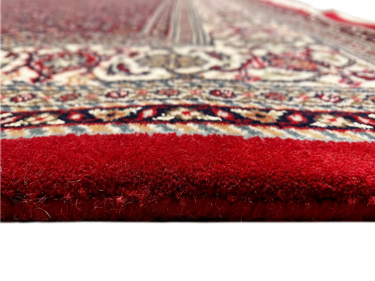 Nahaufnahme der Teppichoberfläche: roter Flor und gemustere Bordüre am Rand