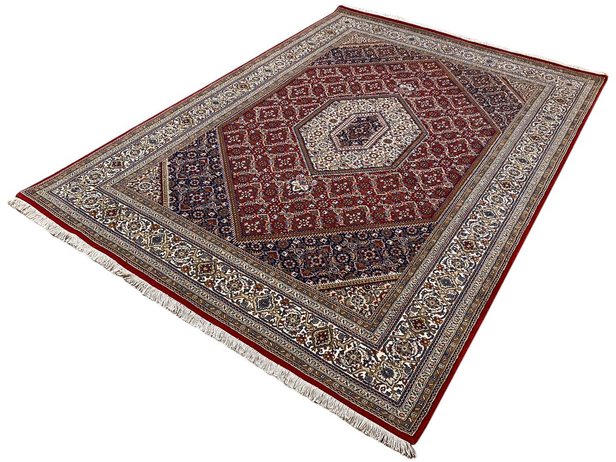 Teppich mit rotem Zentrum, dunklem Außenfeld und ornamentaler Bordüre mit Fransen