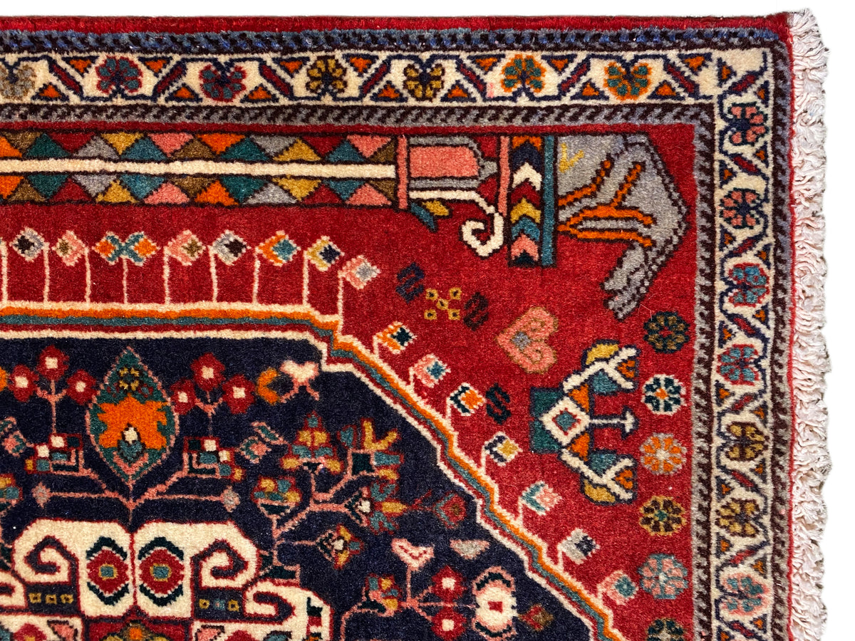 Teppich-Detail: rotes und blaues Ornamentfeld mit mehrfarbiger Bordüre und Fransen