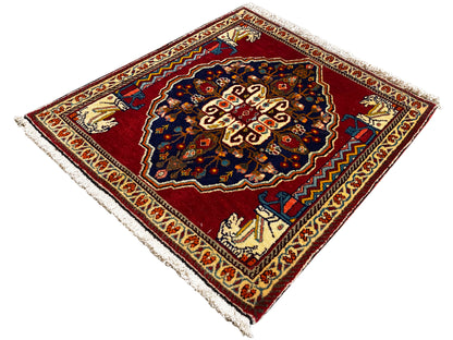 Teppich mit rotem Grund, dunkelblauem Mittelmotiv, beigen Ornamentleisten und Fransen